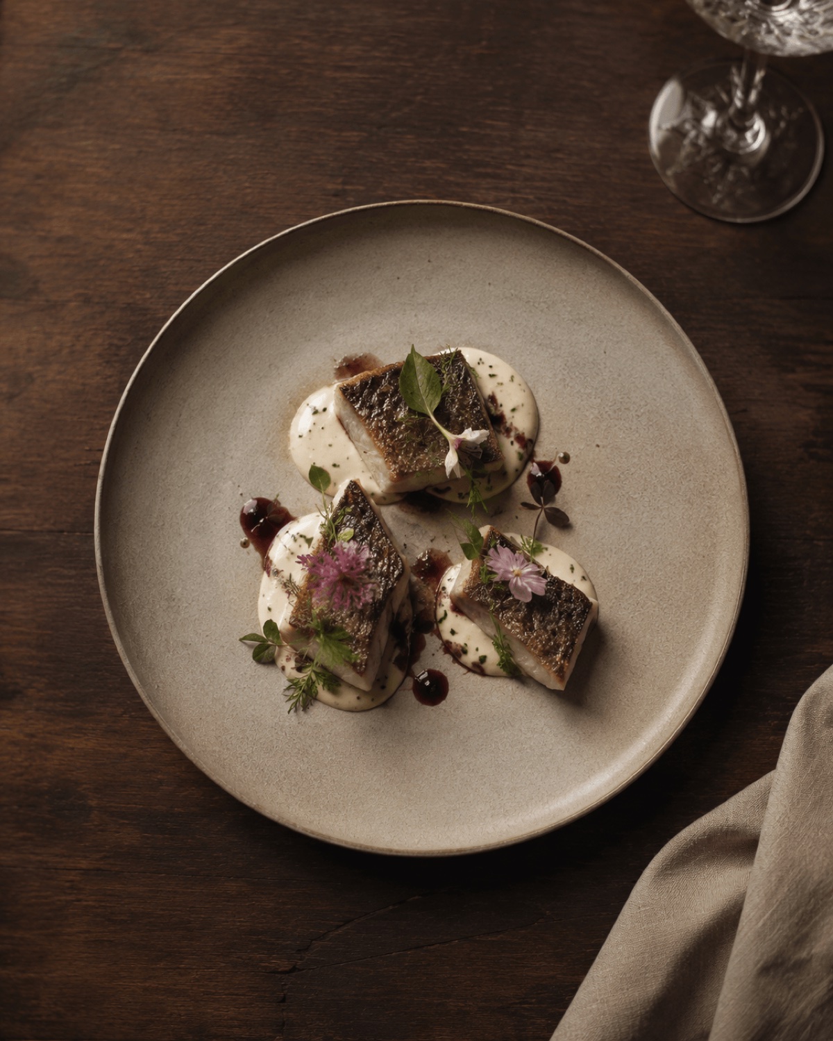 Editorial gestaltete Food-Fotografie eines Fine-Dining-Tellers mit Fischfilet, essbaren Blüten und Sauce — Beispiel für die kuratierte Bildsprache, die Premium-Gäste sofort als professionell erkennen